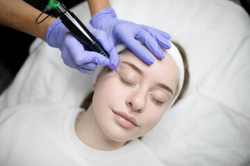 Naklejka premium A woman relaxes while receiving a long-lasting makeup treatment at a beauty salon. The skilled technician uses a device for precise application, enhancing her features for a polished look.