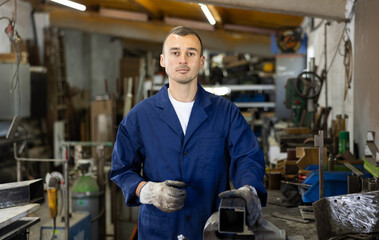 Male welder standing with a welding semi-automatic machine and a safety helmet in a metal machining workshop