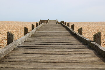 Wooden walkway leading across pebble beach to sea in the distance