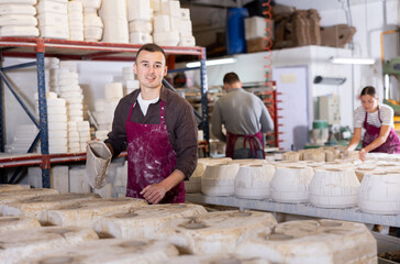 Engrossed in craft, young adult potter meticulously pouring slip into molds, employing slipcasting...