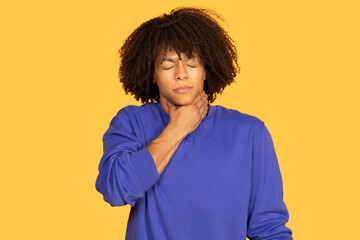A young man with curly hair and a blue shirt is standing against a bright yellow background,...