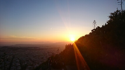 Athens, Greece - 30.3.2018: The sun falling behind the hillside of Lykavittos Hill with the urban skyline with Panathenaic Stadium in sight and the Aegean Sea at the horizon during sunset in spring