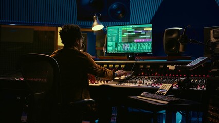Tracking engineer working on a new album and recording hit song, handling mixing console with...
