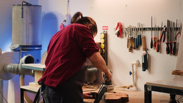 African american carpenter in joinery watching apprentice using orbital sander on lumber. Team in woodworking shop using angle grinder to create wooden decorations, refining wood objects, camera A