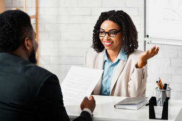 Friendly personnel manager interviewing black candidate during job interview at modern office,...