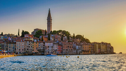 Fototapeta premium As the sun dips below the horizon, Rovinj Croatia waterfront comes alive with warm hues, showcasing colorful buildings, a towering church, and tranquil waters inviting exploration 