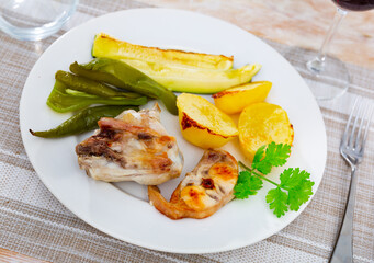Appetizing pieces of baked rabbit with potatoes and vegetables. Decorated with a sprig of fresh...