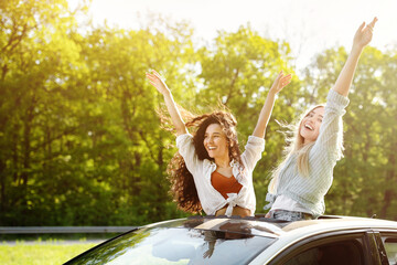 Obraz premium Joyful young friends having fun in their car, partying during road trip, traveling in countryside on summer vacation. Happy multiracial students driving along highway. Hitchhiking concept