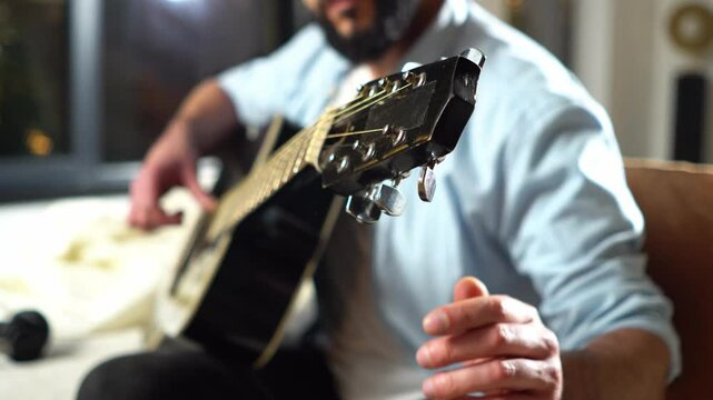 bearded man tunes acoustic guitar and checks the sound, musician repairs his musical instrument and tightens the strings