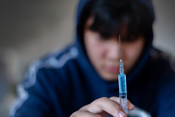 Asian teenboy holding needle which has liquid of drug, soft focus, concept for drug addiction of...