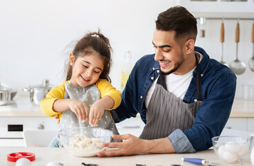 Happy middle eastern father and daughter preparing dough for cookies together, cheerful arab dad...