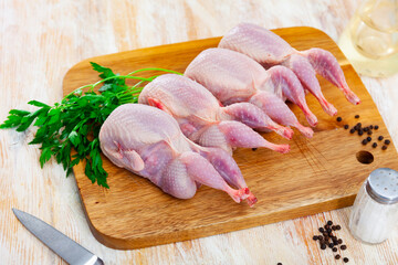 Quail carcasses lie on a cutting board. Small birds are prepared for cooking