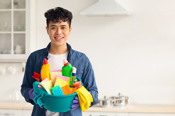 Smiling asian guy house-keeper cleaning apartment, holding spray bottle and other cleaning tools,...