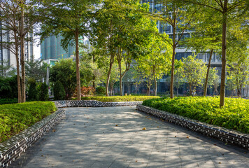 Urban green space or public park features a paved walkway or plaza surrounded by lush greenery,...