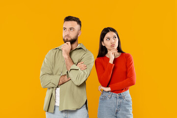 Fototapeta premium A young couple stands together, showcasing affection and contemplation. They pose thoughtfully with curious expressions, dressed in casual attire, against a vibrant yellow backdrop.