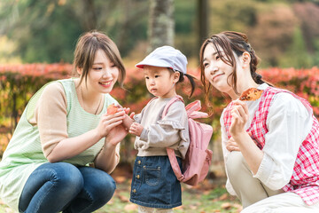 Obraz premium 秋の公園を散歩・遠足する保育士の女性と園児（保育園・幼稚園保母・子供・幼児） 
