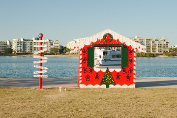 Wide Framed view through a red, white and green Christmas photo booth.  Large white boat in the frame with Boca Ciega Bay in back. At St Pete Beach, FL. Blue Sky and calm water. 
