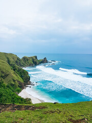 Idyllic landscape of green hills merging into the ocean, where waves gently roll toward the shore...