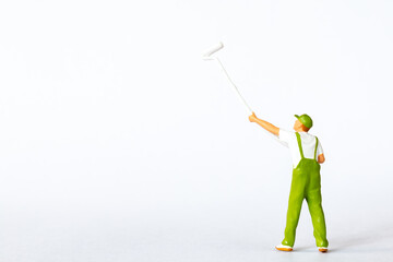 A miniature figure of a painter using a long roller brush to paint on a white background