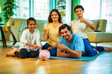 Happy Indian family promoting saving habits, pointing at a piggy bank during quality time at home