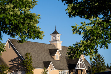 Classic building with cupolas, asphalt roof shingles, and clocktower on a sunny blue sky day
