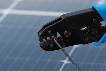 Close-up of a technician using a crimping tool to connect wires on a solar panel during installation at a renewable energy site.