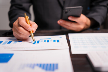 A young Asian man in a formal suit works late at night at his desk, analyzing stock market charts on a laptop and tablet, ensuring accuracy in financial data analysis.