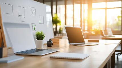 A modern workspace featuring laptops, a camera, and a whiteboard in a sunlit environment.