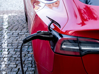 EV car charger handle plugged in, electric vehicle charging cable, recharging battery on modern red...