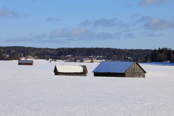 Three wooden barns in snow covered field on a sunny day of winter.
