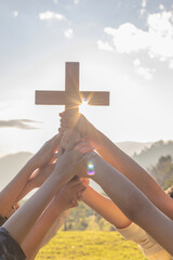 Friendship hands praying and holding Christian cross for worshipping God on mountain at sunrise...