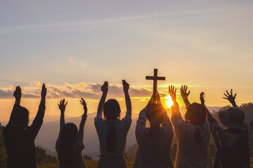 Silhouette of group children praying to the GOD while holding a crucifix symbol with bright sunbeam sunset sky background