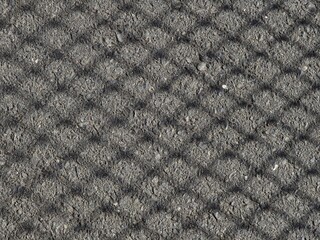 Shadow of a chain-link fence cast on a rough asphalt road, forming a diamond-shaped pattern on the...