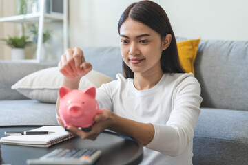 Saving money wealth concept, asian young business woman hand putting coin into piggy for saving cost, cash finance planning to spend enough money on her income for save money, payment tax, investing.