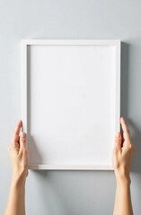 Female hands hanging empty white wooden blank frame mockup on white wall