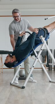 People, stretching and exercise as physiotherapist for fitness, wellness and strong muscle. Men, inversion table and coach for back pain, support and recovery in physiotherapy, workout and healthcare