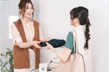 アパレルショップで購入を決めてレジの店員にデニムを渡す女性客
