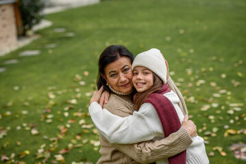 Young granddaughter with gradmother hugging, standing in garden.