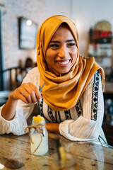 Muslim woman enjoying lemonade in cafe: smiling in hijab