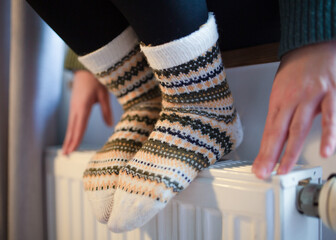 The girl's hands and feet are in warm socks. a young girl sits by the window and warms herself from the heating radiator. Heating in an apartment, house. 