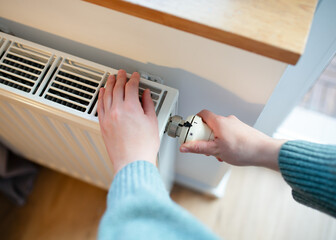 Woman warms up hands over heater. Concept of the need for good central heating.