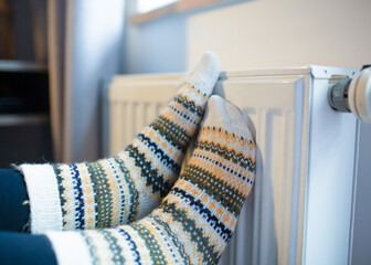 Woman with her feet resting on a radiator to warm them up by the cold of winter and energy saving.