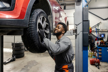 Hardworking multicultural car mechanic standing at car workshop and changing tires.