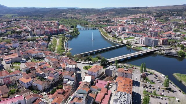 Scenic drone view of Mirandela, small Portuguese city on banks of Tua overlooking terracotta roofs of residential buildings and two bridges across river on sunny spring day