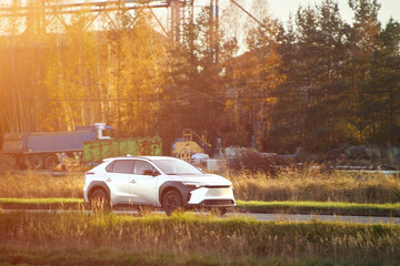 White hybrid vehicle driving near autumn trees