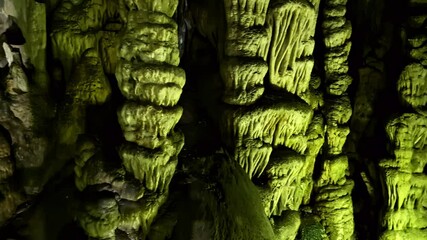 Stalactites and stalagmites glow under green light in a mysterious limestone cave in Greece