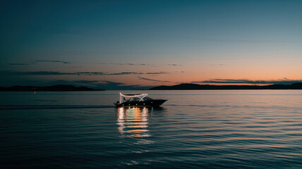 Serene Evening Scene Over Calm Water with Illuminated Boat and Gentle Reflection, Horizon Gradient from Deep Blue to Soft Orange, Silhouettes of Distant Landforms, Clear Sky with Scattered Clouds