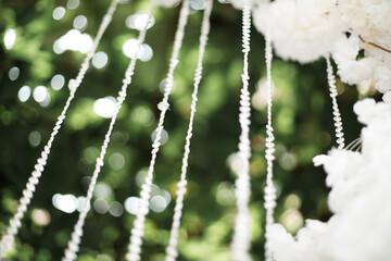 several vertical strands with white beads hanging from the top. In the background there is a blurry background with green tints