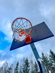 Basketball Hoop with Snow-Covered Ball Against Winter Sky. High quality photo