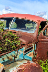 A rusted old car is sitting in a field with weeds growing around it